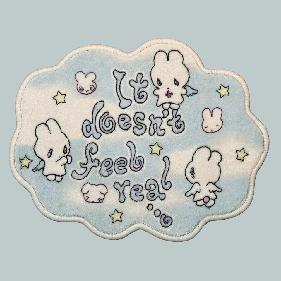 Embroidered patch with cartoon characters and text 'It doesn't feel real' on a wooden surface