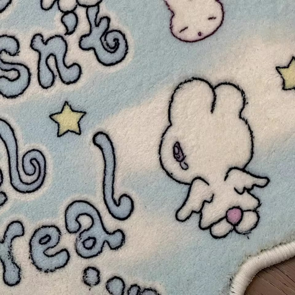 Close-up of a soft toy with a cartoon character on a fabric surface with text and stars.