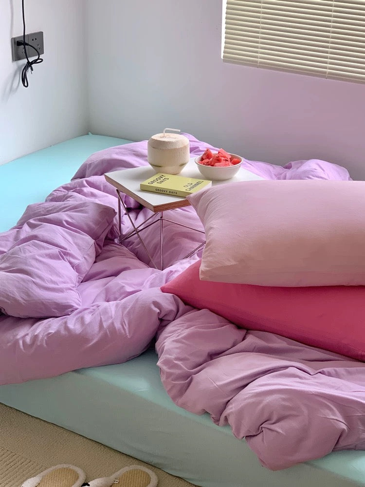 Bed with pink bedding and a small table with items on it, in a room with light blue walls.