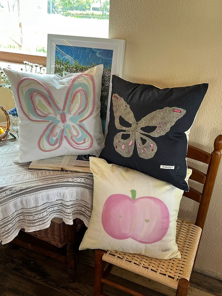 Pastel dorm throw pillows with butterfly and apple oil painting designs on a lace covered table