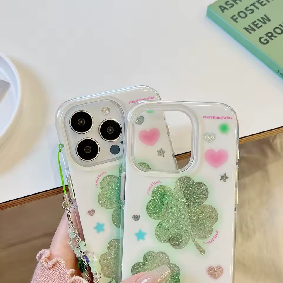 Two phone cases with clover and heart designs held by a hand.