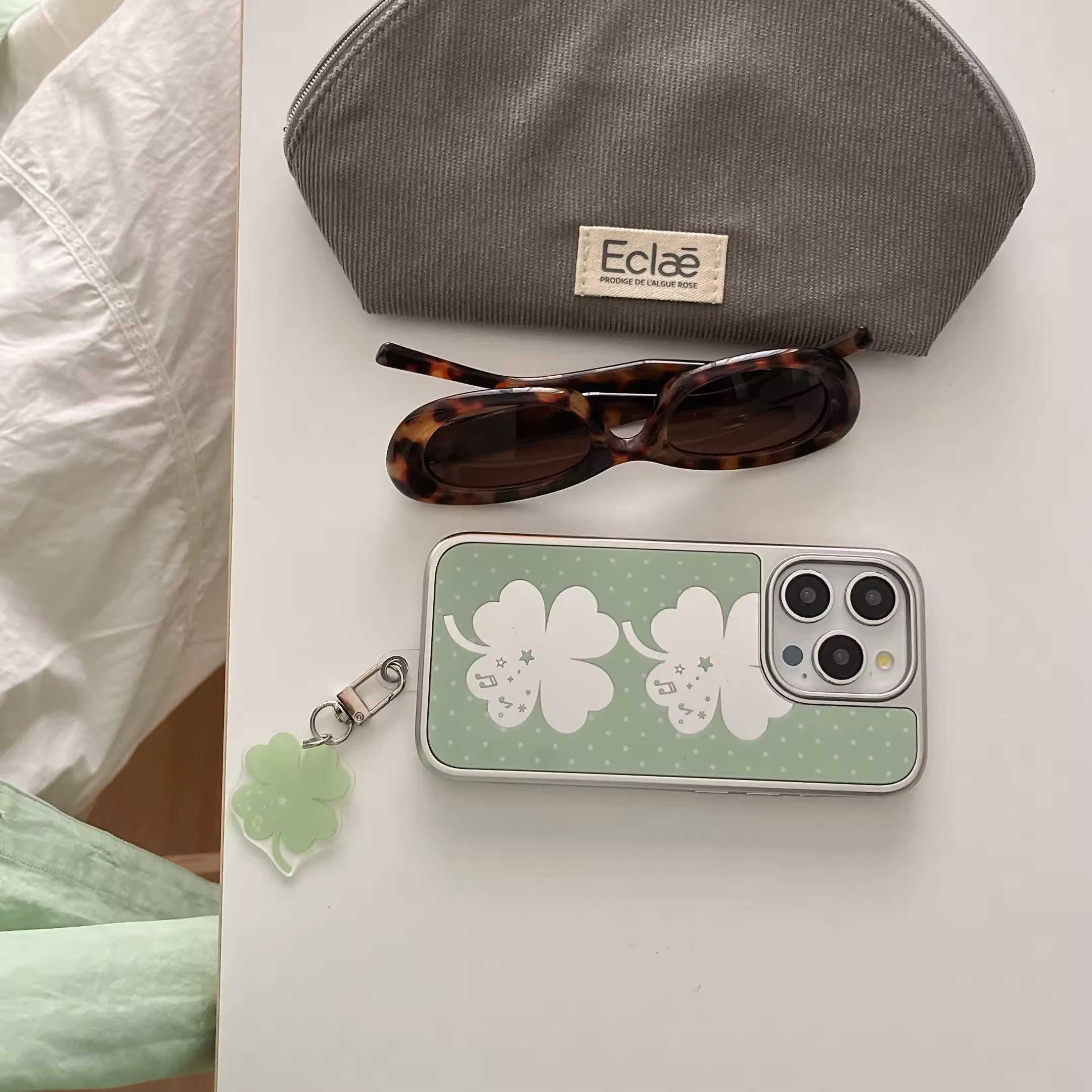 Green mirror iPhone case with clover pendant placed on aesthetic pastel desk