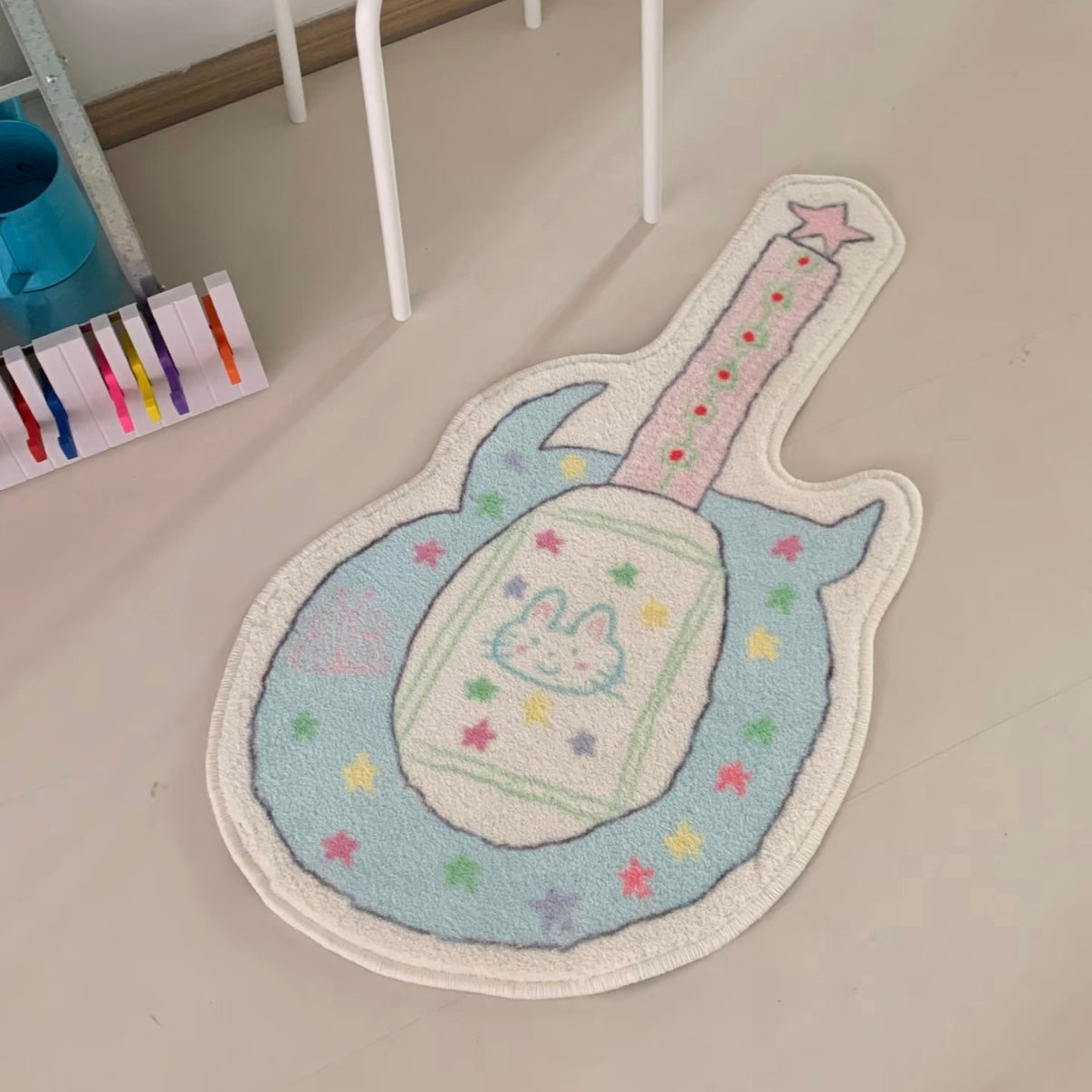 A guitar-shaped plush rug with a pastel design, featuring a bunny face on the body and colorful star accents, placed on a light beige floor.