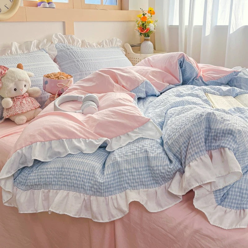 Bed with pink and blue checkered bedding, teddy bear, and small basket in a bright room.