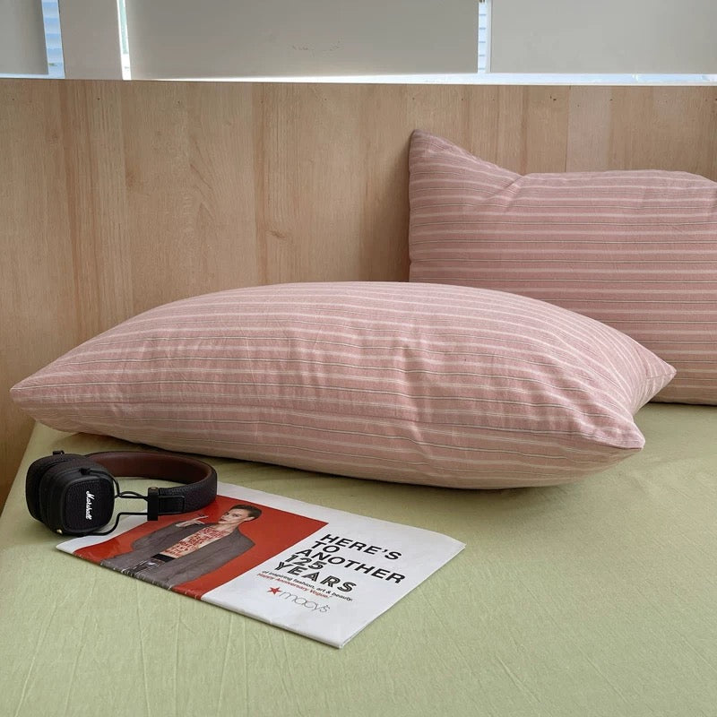 Pink striped pillows on a bed with a magazine and headphones.