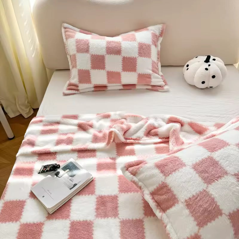 Pink and white checkered blanket and pillow on a bed with a small plush toy.