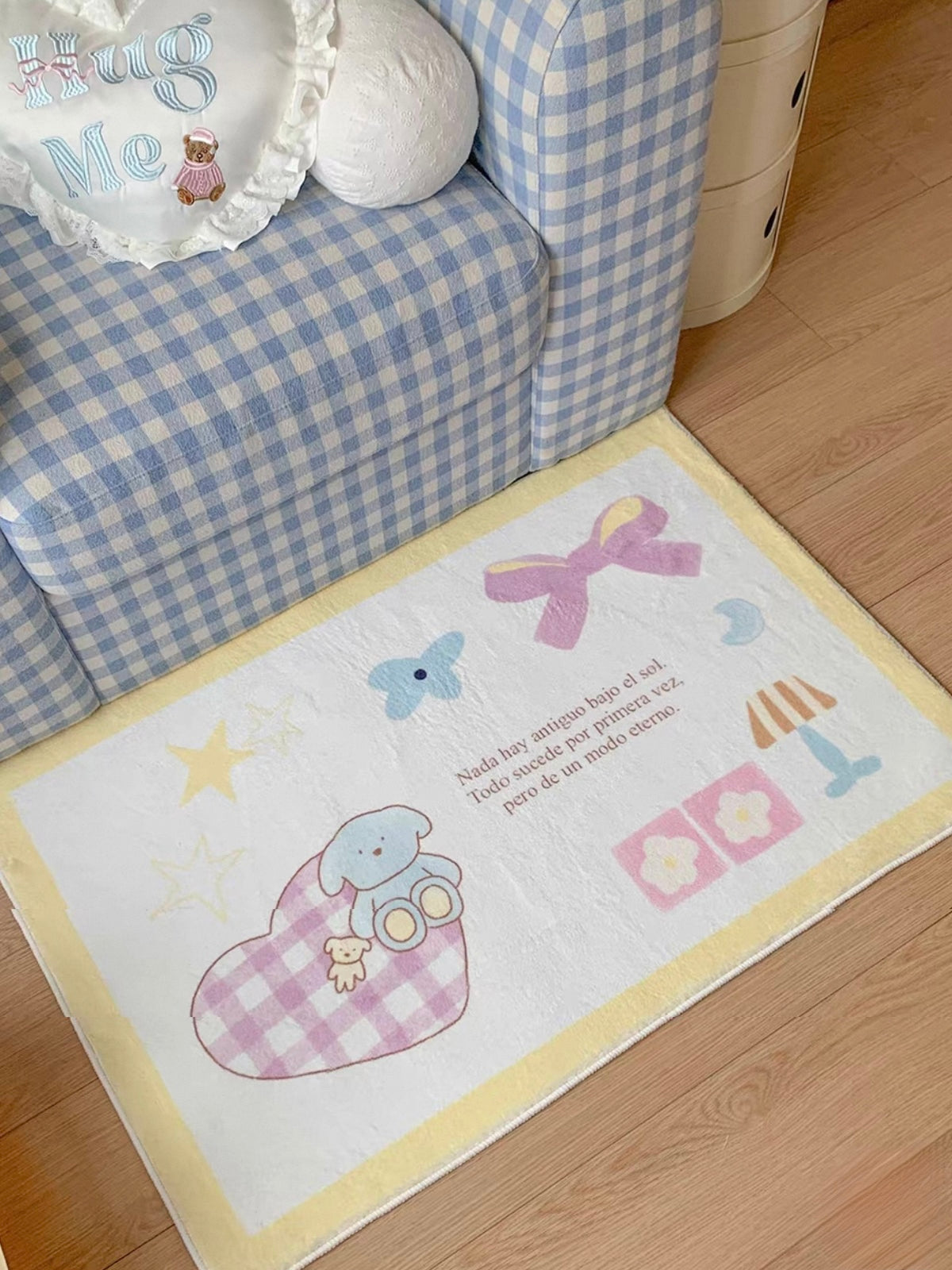 A pastel rug with a yellow border lies in front of a checked armchair, showing its elephant, bow and heart artwork.