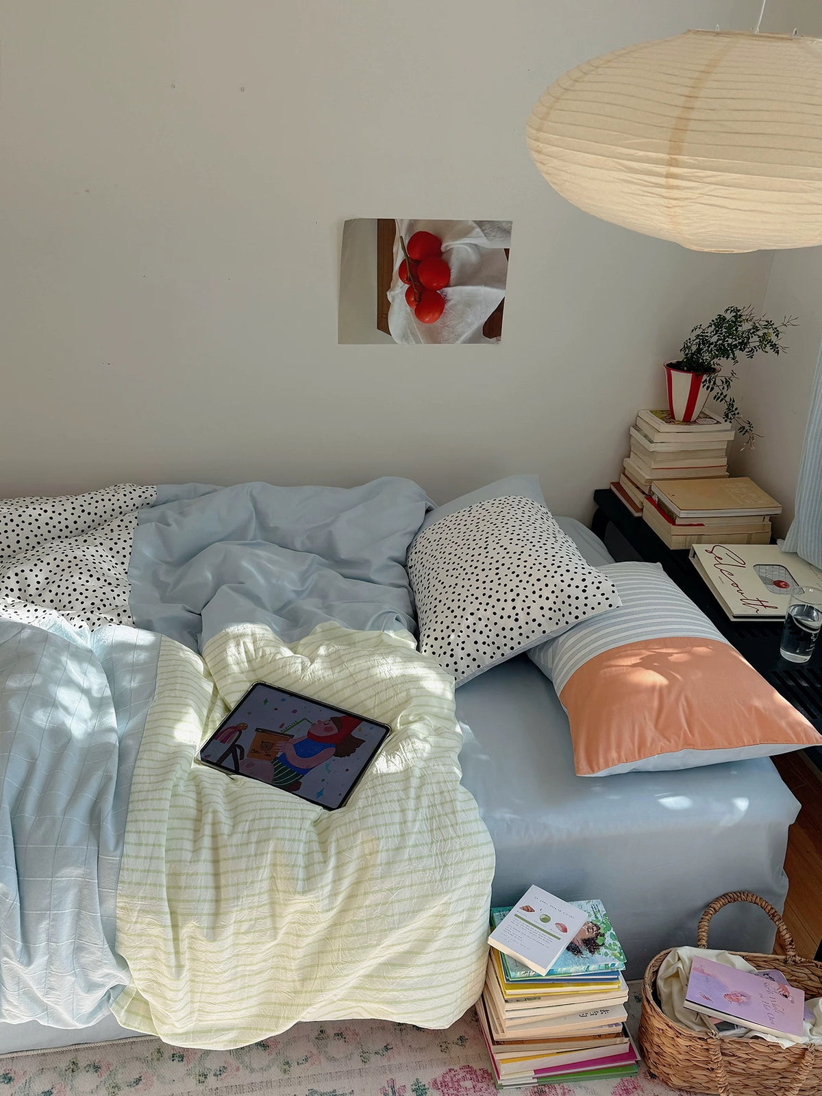 Pastel textured bedding in pale blue and yellow covers a bed beneath a large paper lampshade.