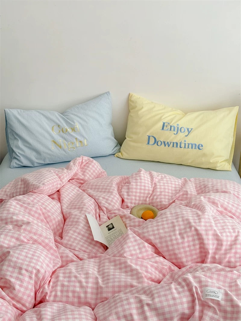 Pink checkered comforter on a bed with pillows and a bottle of wine.