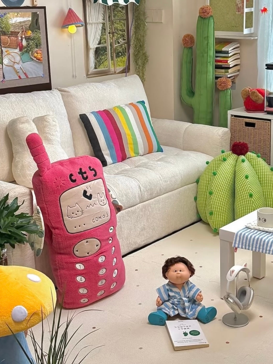 A pink phone shaped pillow stands beside a sofa, showing the long keypad and small antenna in a wide room view.