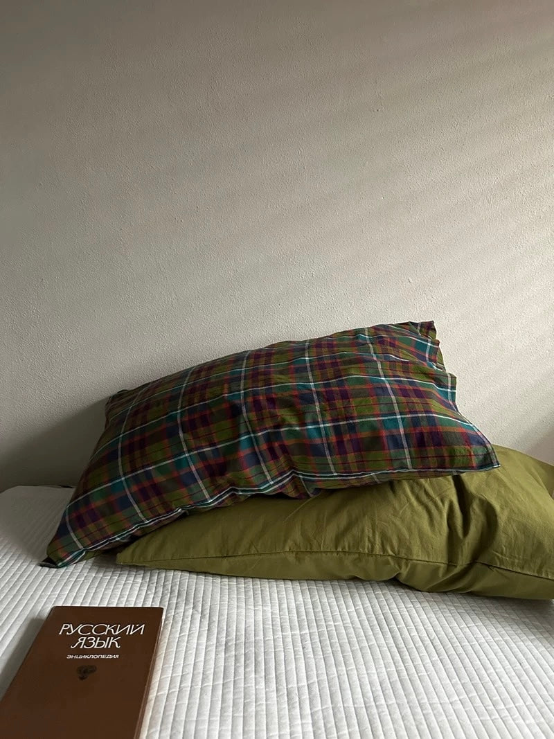 A pillowcase set styled with multicolor plaid resting over olive green on white bedding.