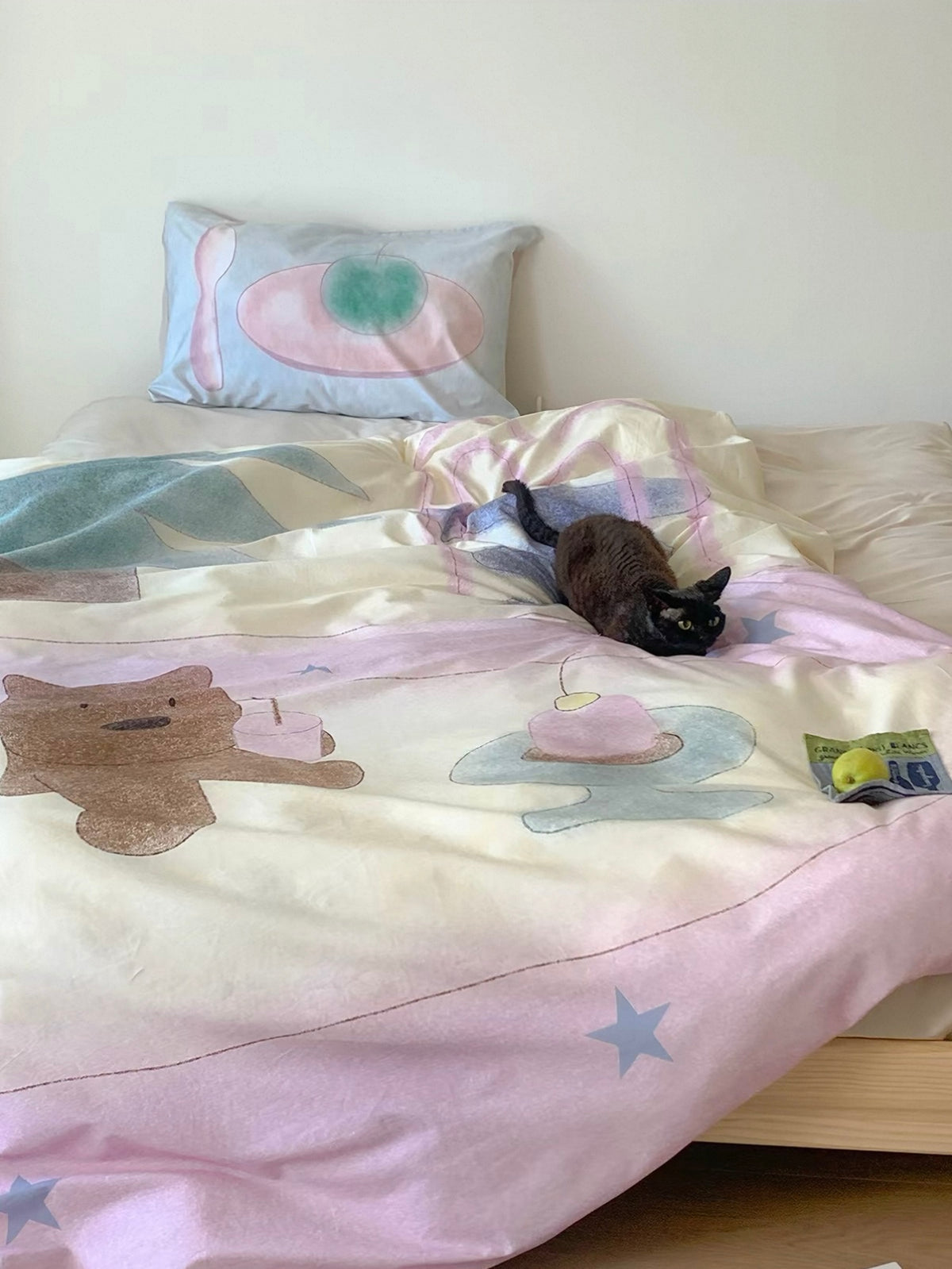 Pastel bear bedding loosely arranged across the bed with headphones and reading items on top.