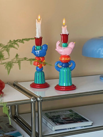 Pink and blue bird candle holders with lit taper candles styled together on a mirrored console.
