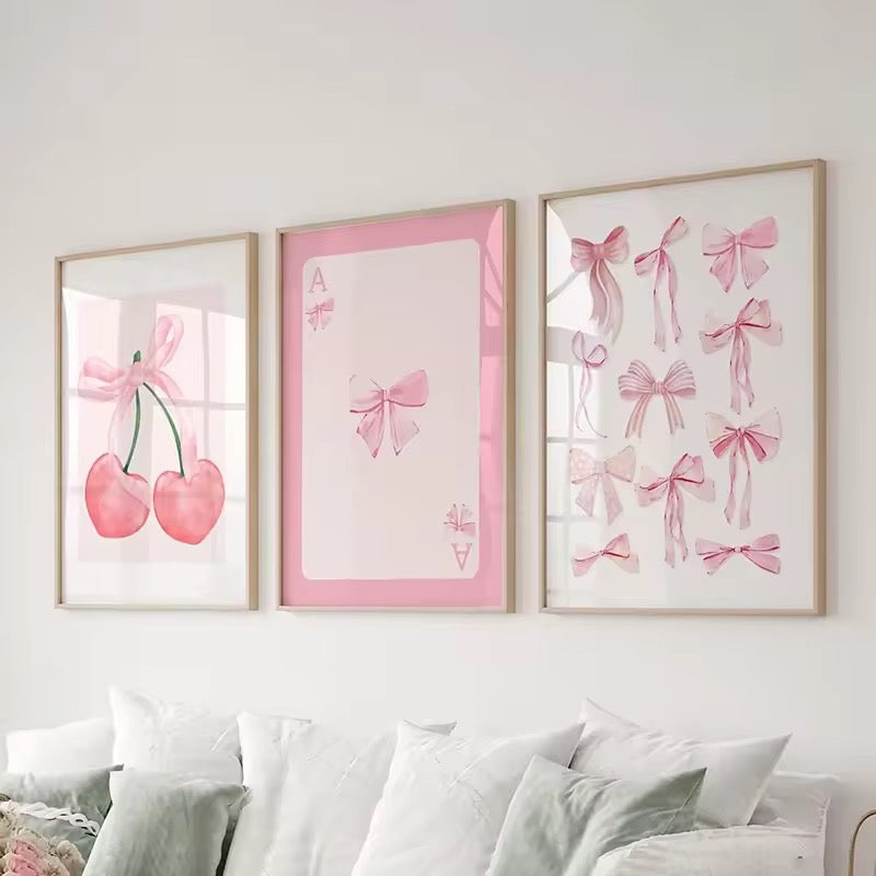 Three pink-themed canvas posters including bows, cherries, and card designs in a soft girl bedroom.