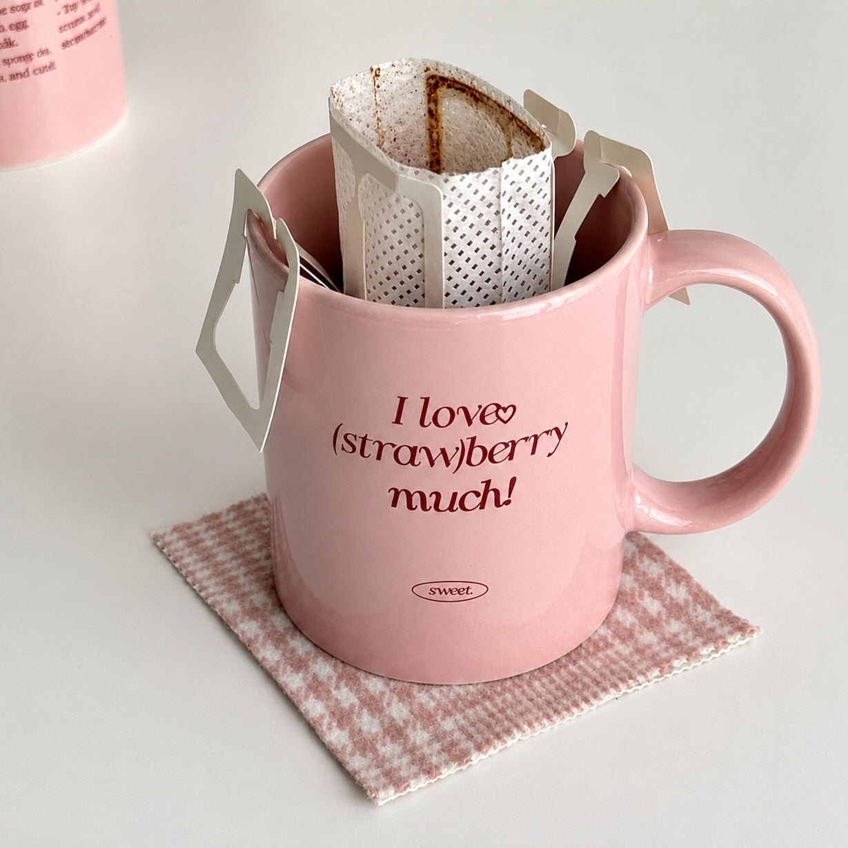 A pink ceramic coffee mug with the text 'I love (strawberry much!)' and a small 'swir.' logo, holding two white paper drip coffee bags.