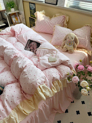 Pink and white polka dot comforter on a bed with pillows and a teddy bear.