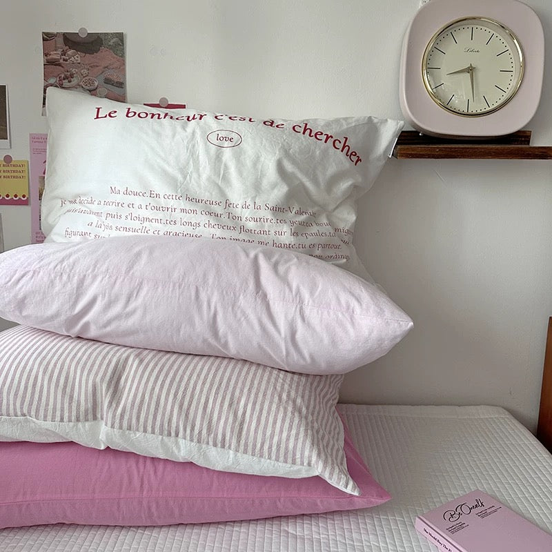 Two pillows with text on a bed next to a clock.