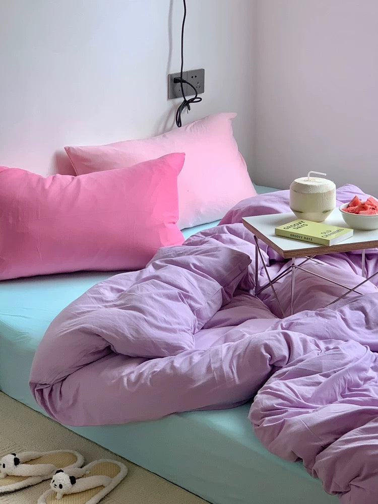 Bed with pink bedding and pillows, a small table with a teapot and bowl on a light blue bedspread.