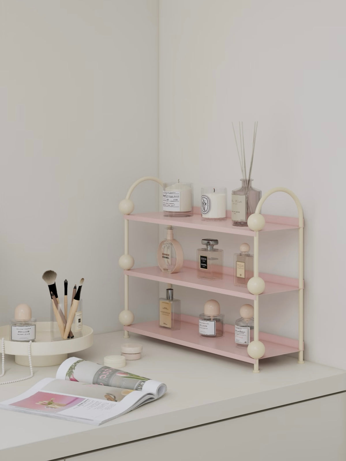 Pink fragrance shelf shown from the side with cream ball details and small containers on its open levels.