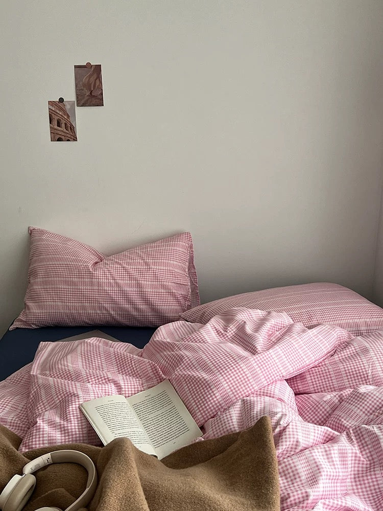 Bed with pink checkered bedding, pillow, and a book on a wooden nightstand.