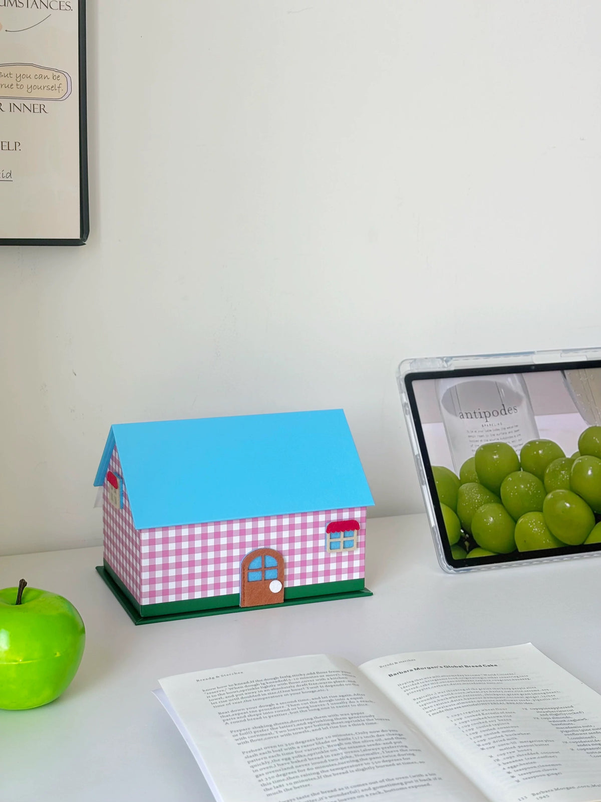 Pink gingham tissue box cover beside an open book and green apple
