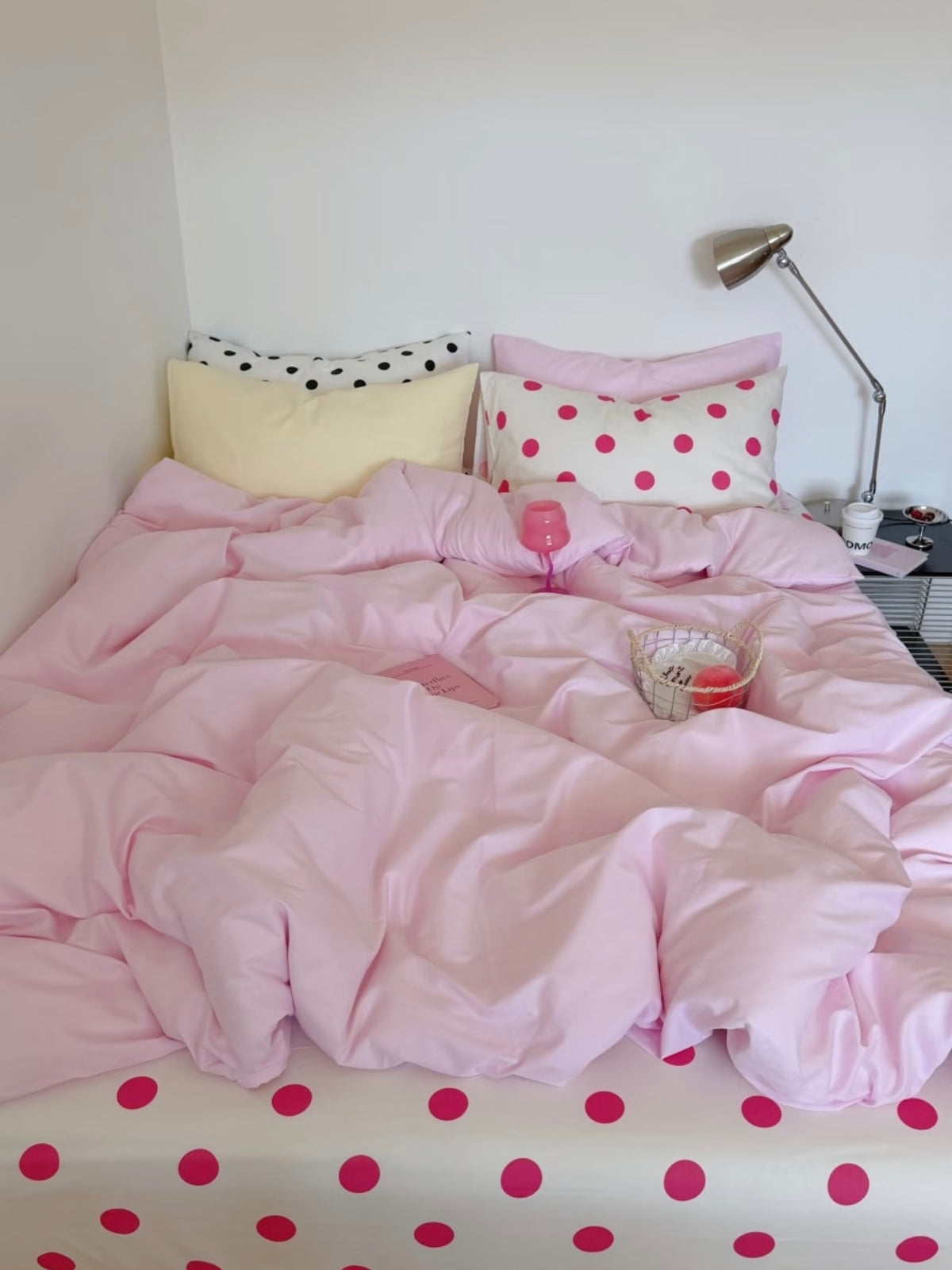 Front view of a pink bedding set with fuchsia dots across the white sheet and contrasting pillows at the head of the bed.