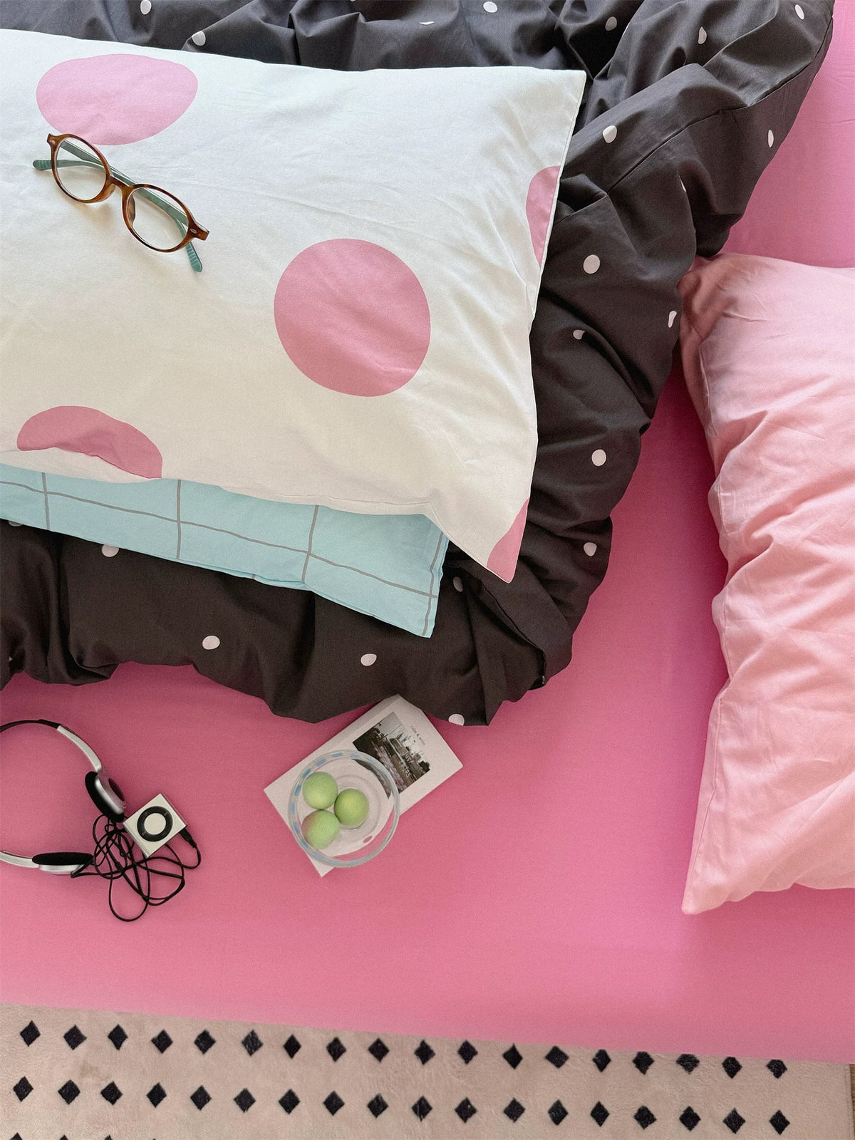 Overhead detail of a pink dotted pillow on blue checks, with the dark cover and plain pink pillow beside it.