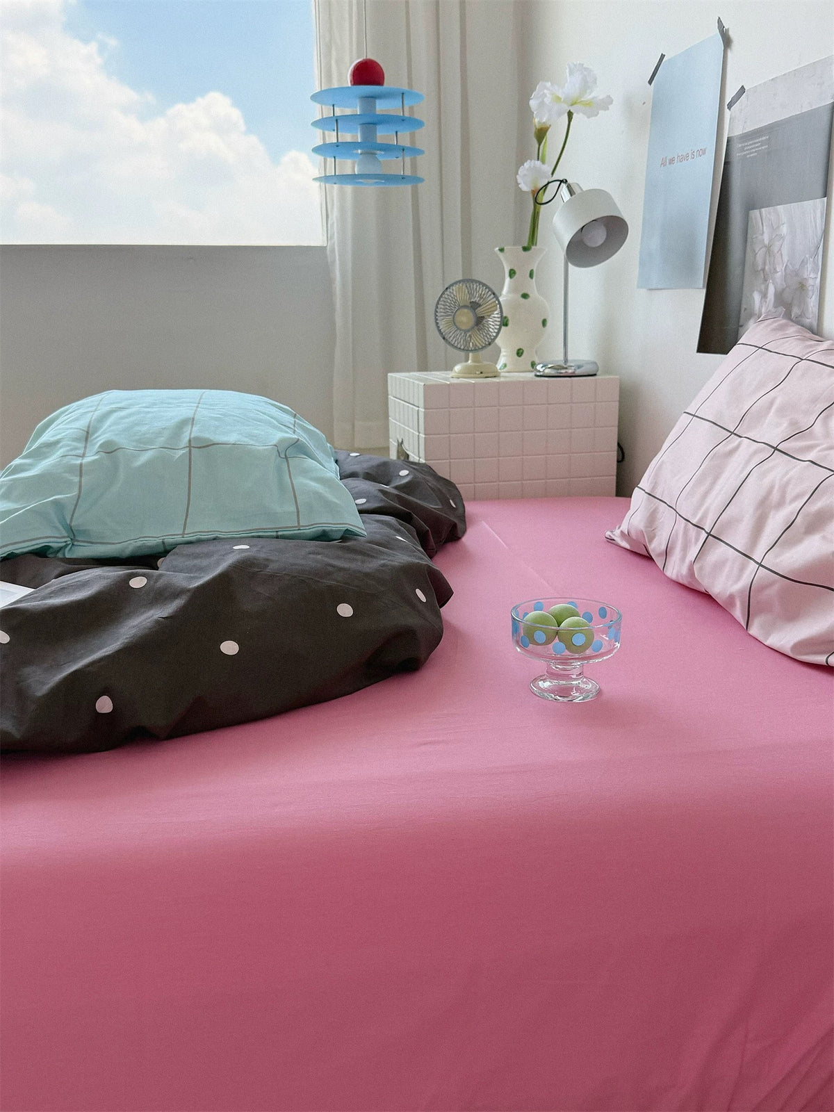 A close view of the pink sheet shows blue and pink checked pillows on either side of the dark dotted cover.