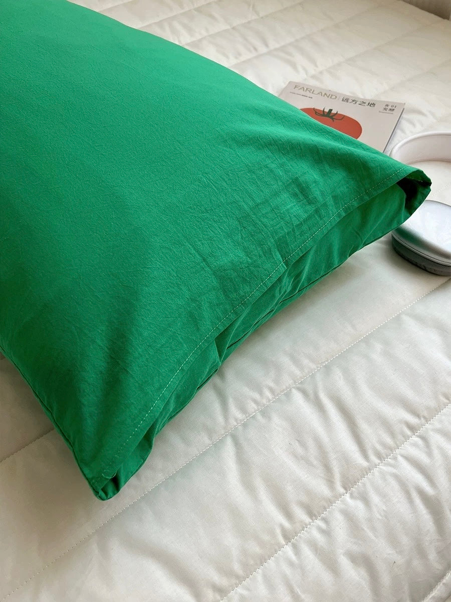 A bright green pillowcase on a white quilted bedspread, with a small magazine and a round container nearby.
