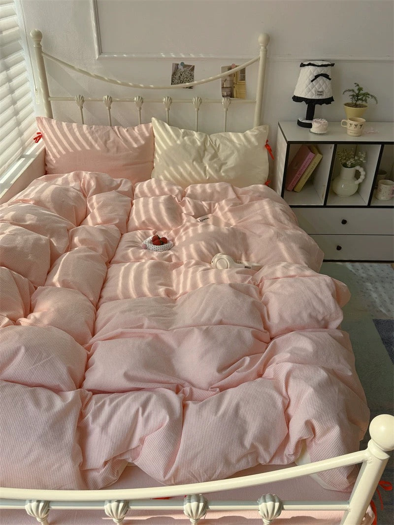Pink comforter on a bed in a room with a nightstand and decor items.