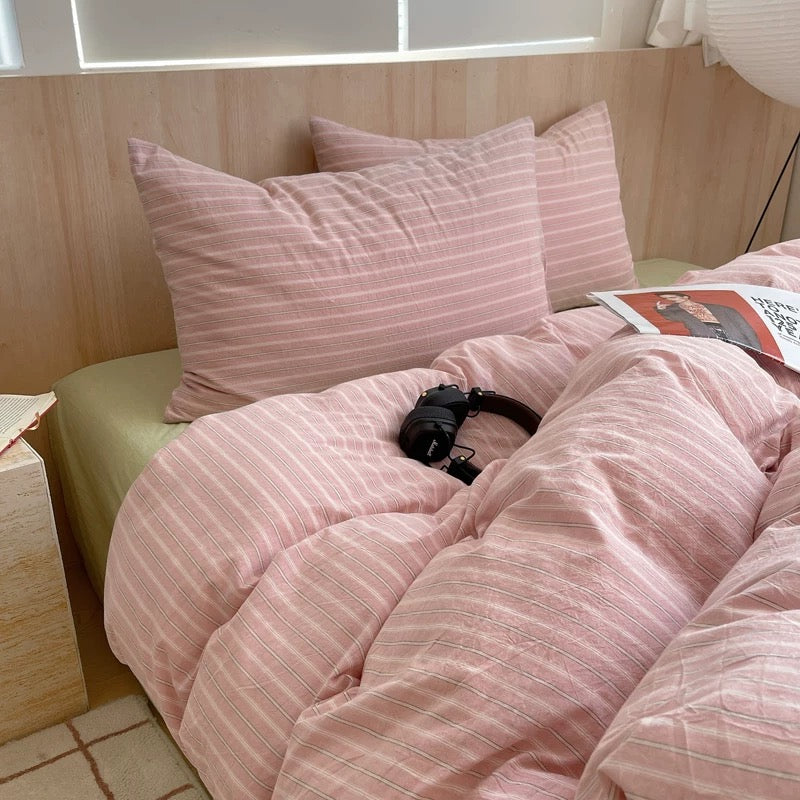 Bed with pink striped bedding and pillows in a room with wooden walls.