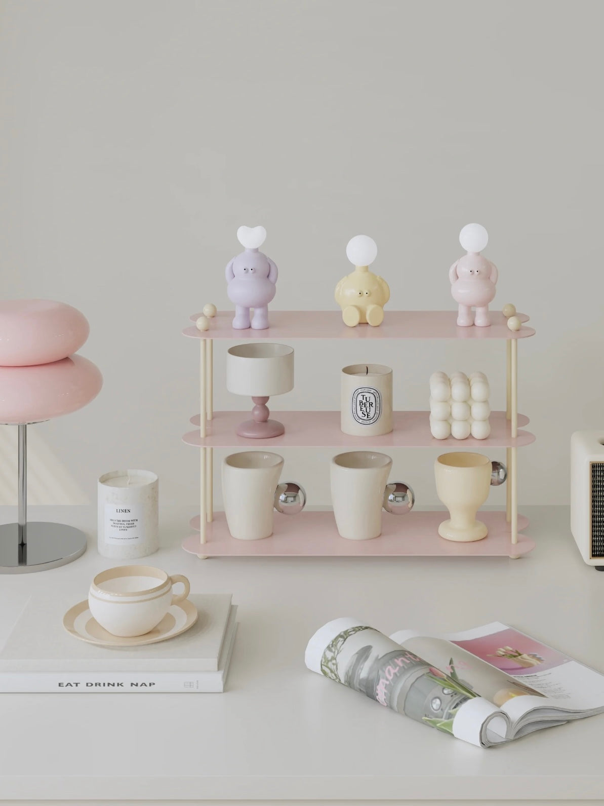 A pink tabletop shelf is shown from the front with cream ball details, cups below and small figures above.