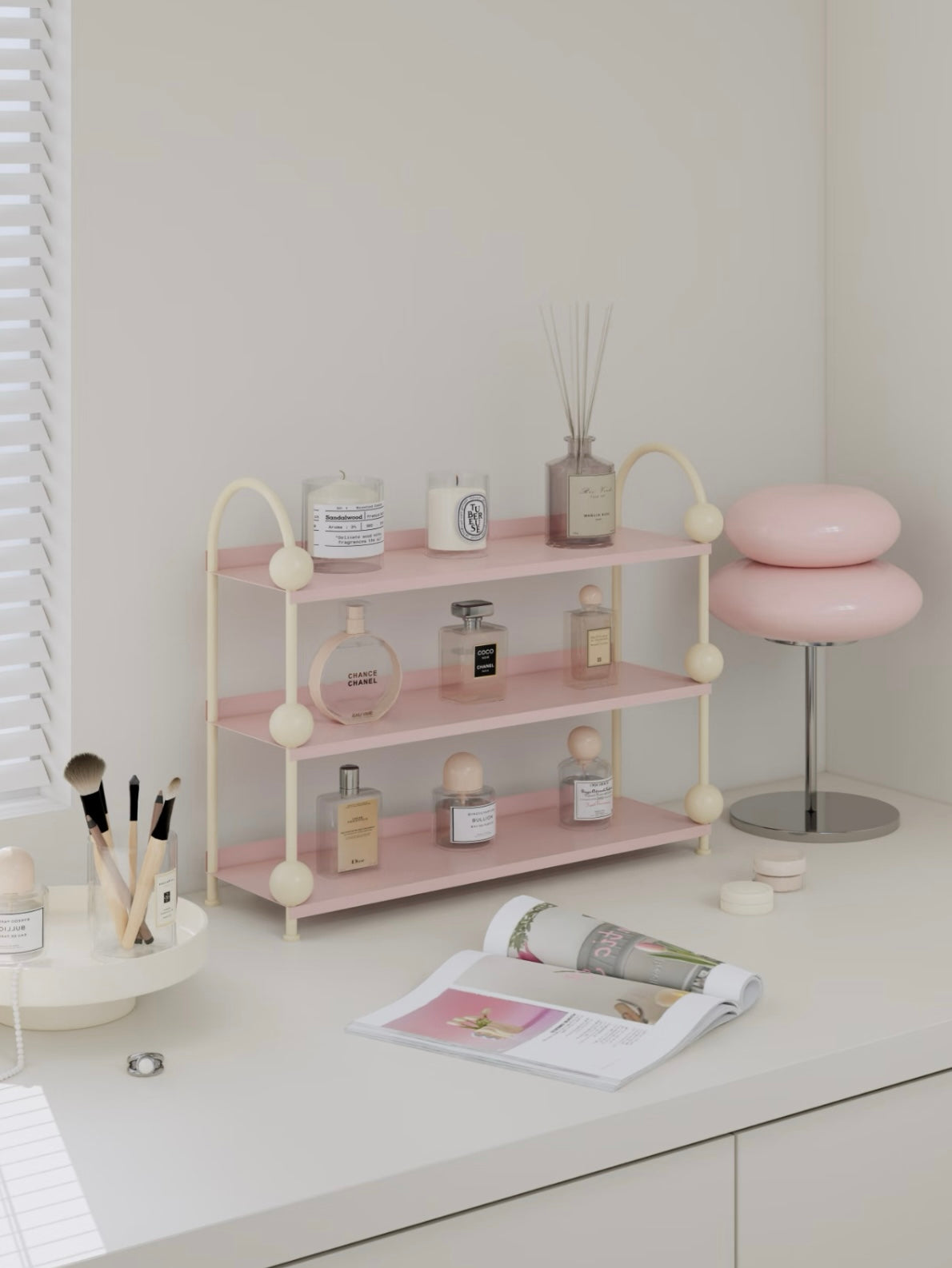 Pink vanity shelf viewed at an angle with cream supports and small bottles arranged on the open tiers.