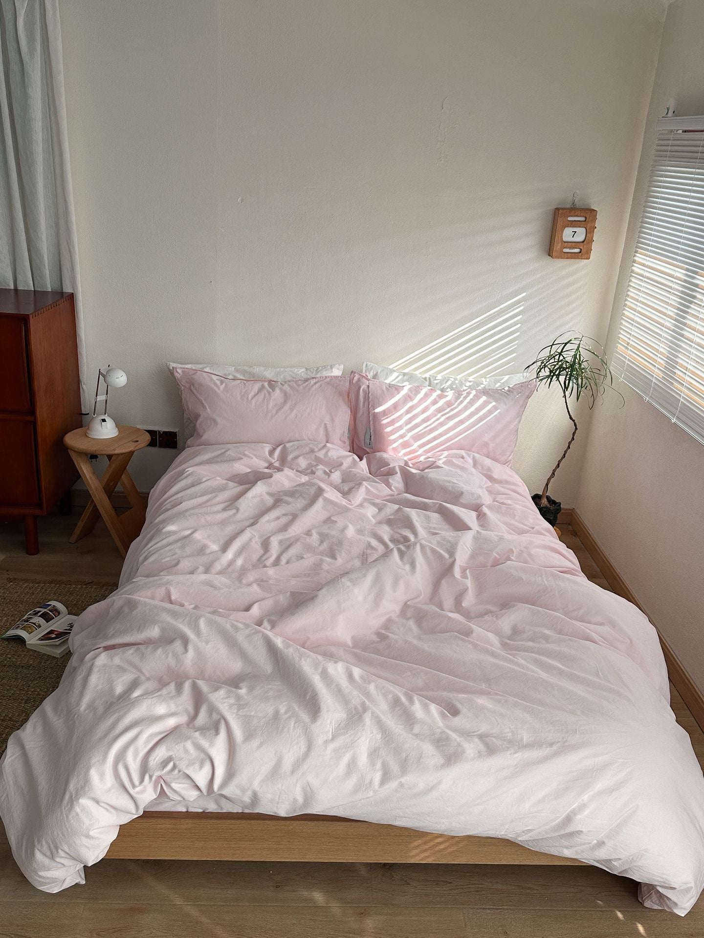 Unmade bed with white bedding in a room with a window and side table.