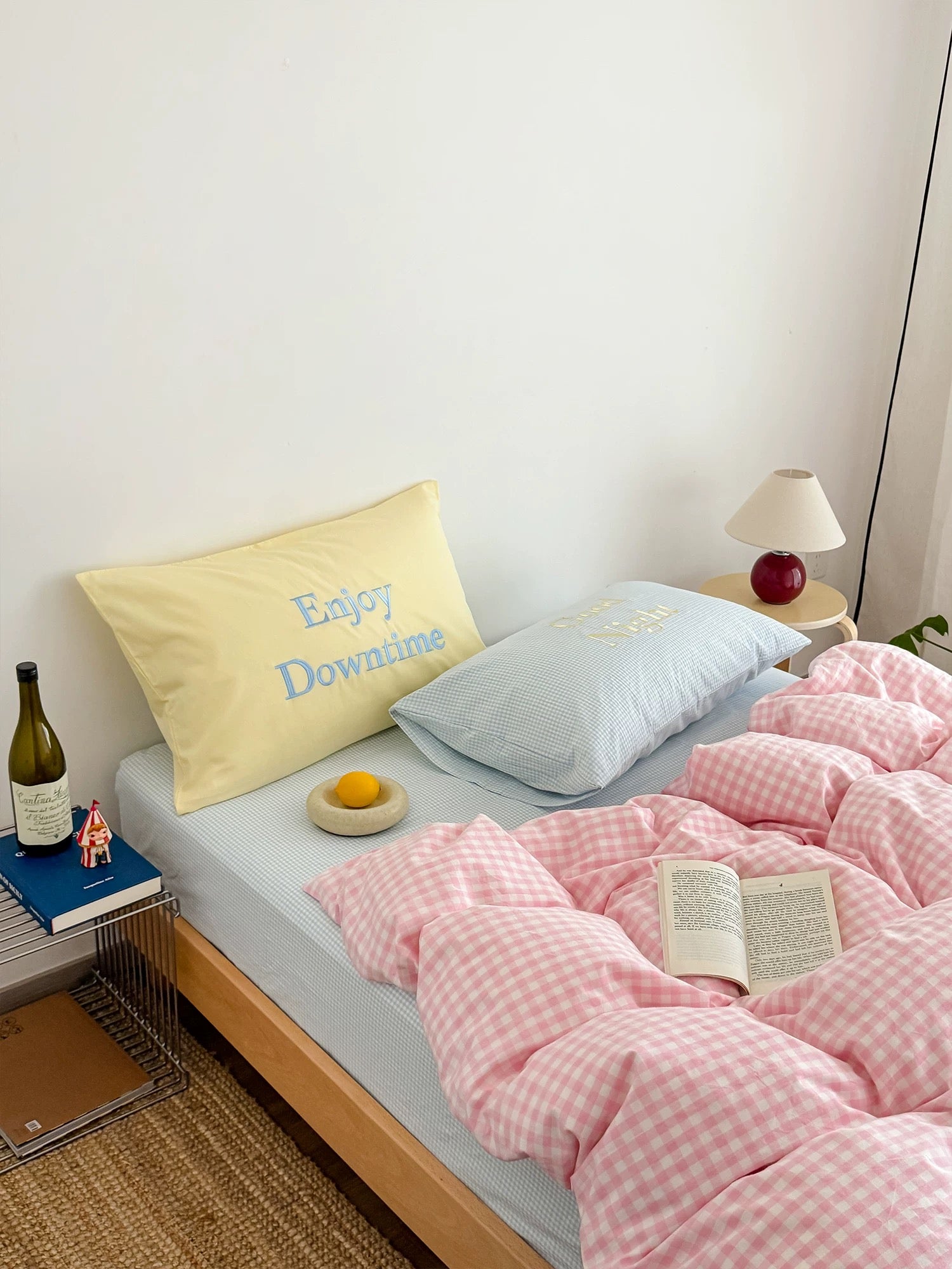 Bed with pink checkered duvet, yellow pillow, and blue pillow with 'Enjoy Downtime' text.