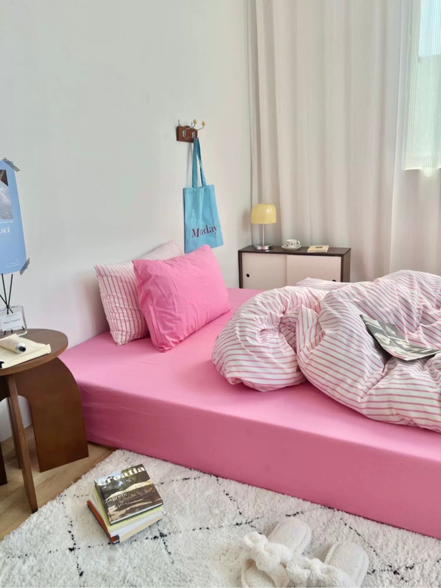 Pink bed with pink pillows and striped blanket in a room with white walls and a small table.