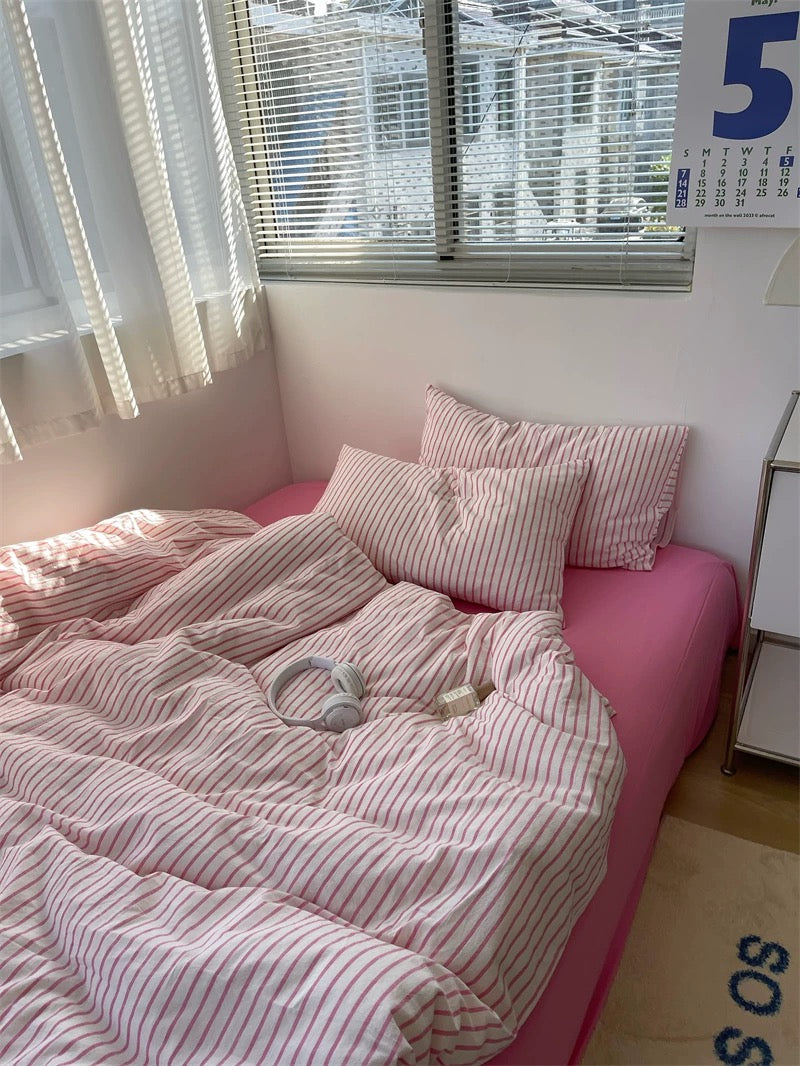 Bed with pink bedding and pillows in a room with a window and calendar.
