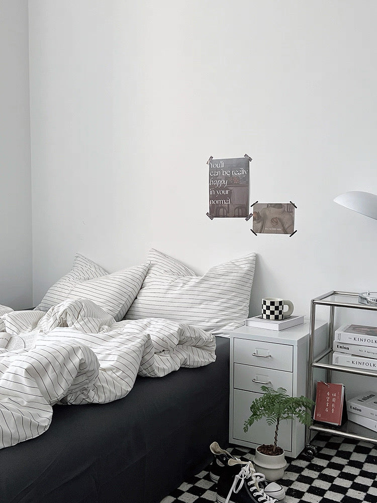 Bedroom with black and white striped bedding, a nightstand with a plant and books, and a checkered floor.