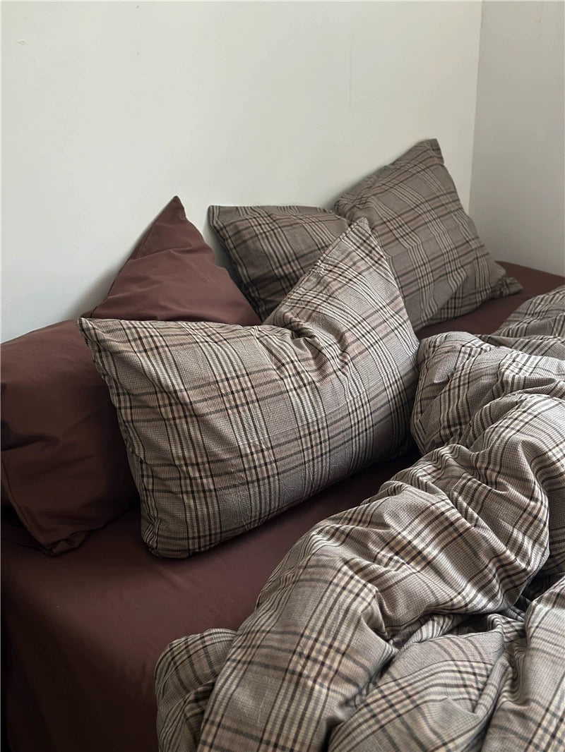 Plaid pillows and blanket on a bed against a white wall