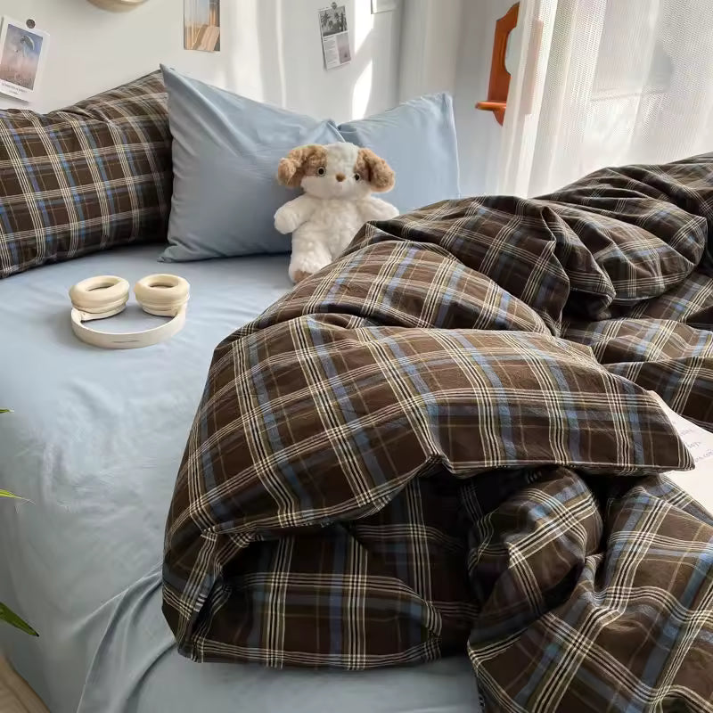 Bed with plaid comforter and pillows, featuring a teddy bear and small bowls.