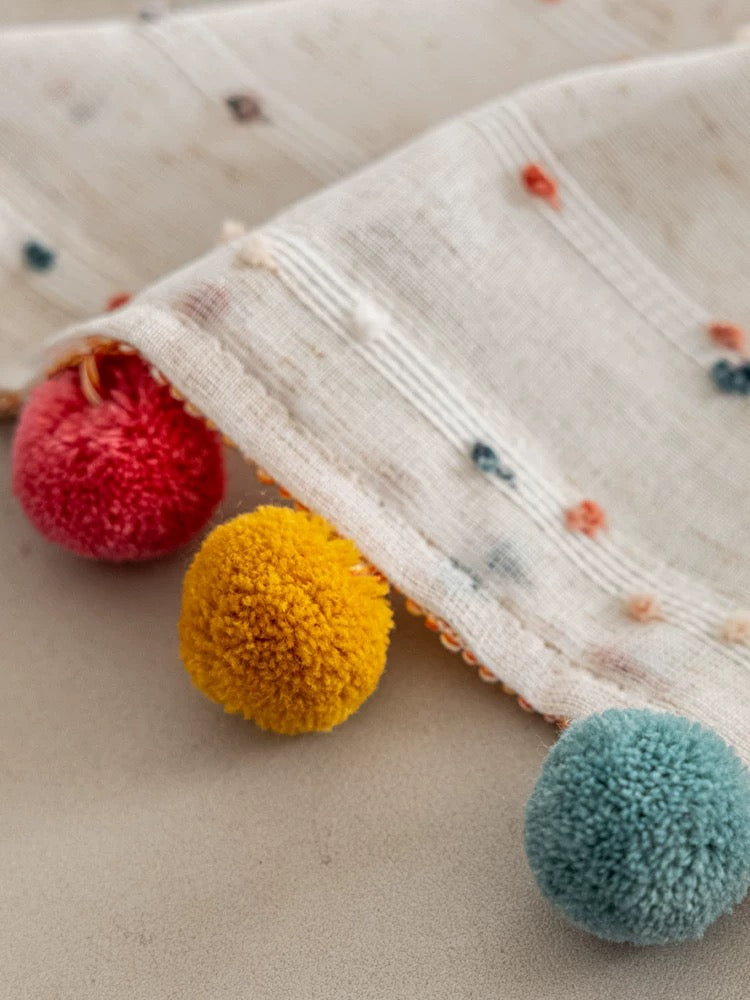 Product flat lay of fabric edge showing stitching and pom-pom quality.