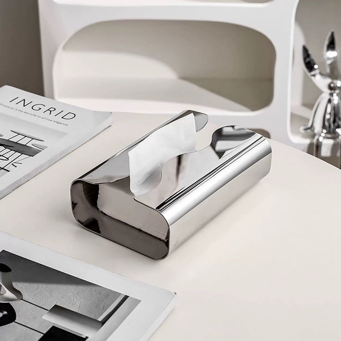 Chrome paper towel holder on a white surface with a magazine underneath