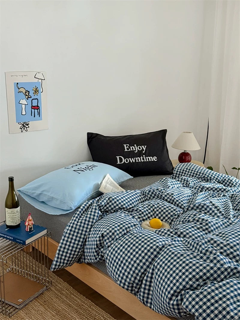 Bedroom with checkered bedding and pillows, including a black pillow with 'Enjoy Downtime' text.