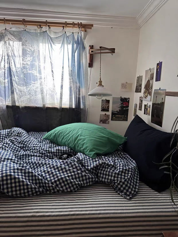 Bedroom with a bed featuring checkered duvet and green pillow, curtains covering a window.