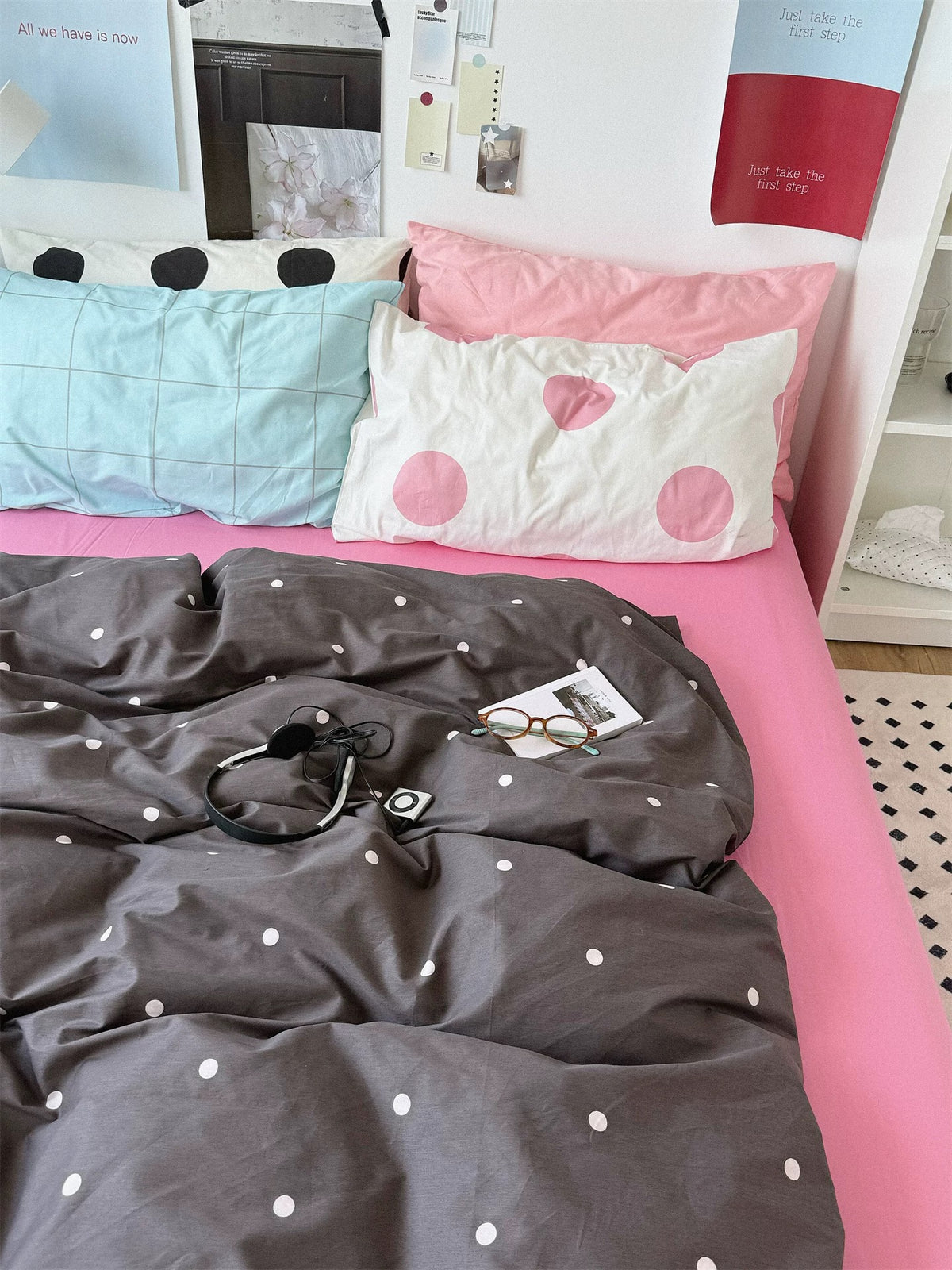 Preppy pink bedding seen closer from the front with a blue checked pillow beside large pink dots and black dots behind.
