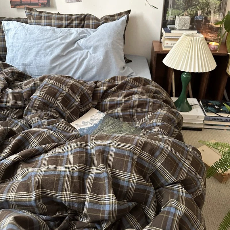 Plaid blanket on a bed with pillows and a lamp in the background