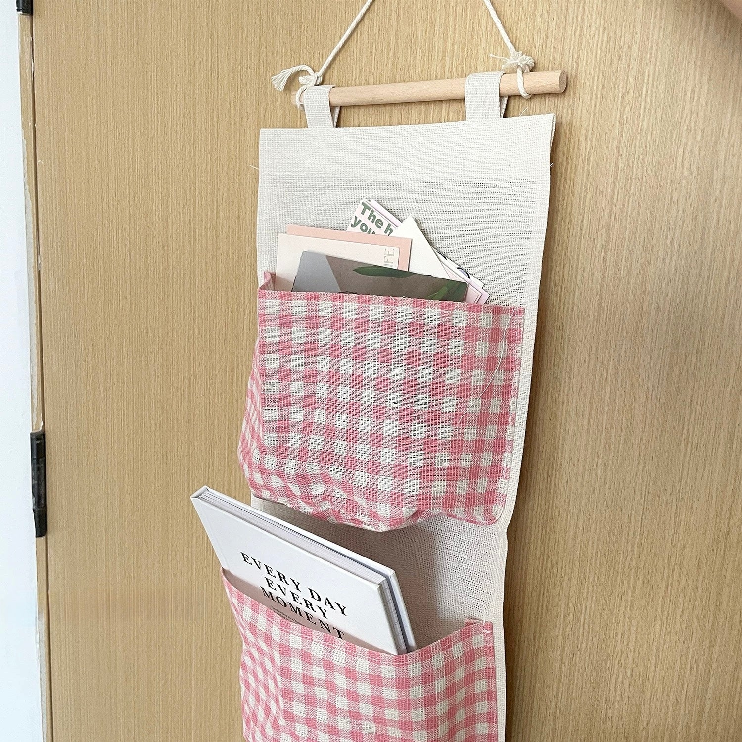 Wall-mounted organizer with pink checkered pockets hanging on a wooden door.