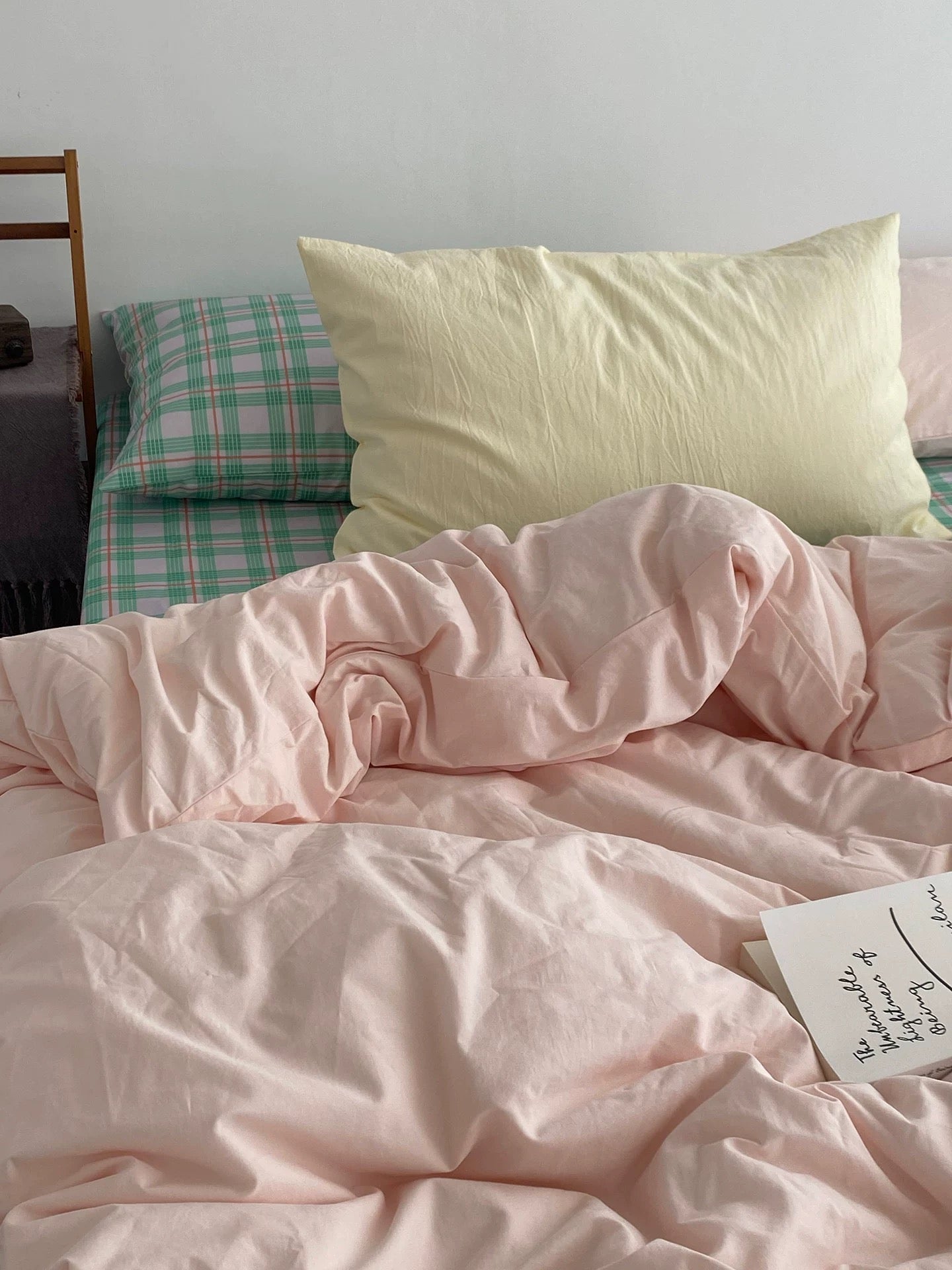 Bed with pink bedding and a yellow pillow against a white wall.