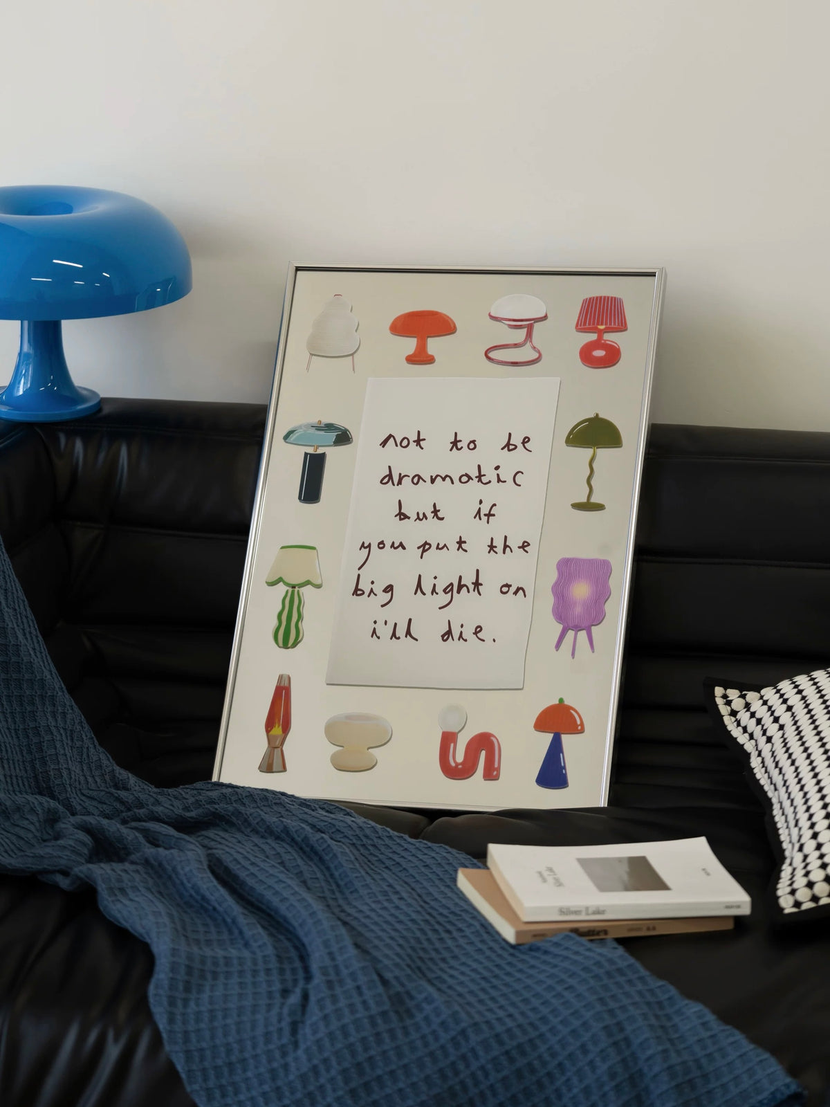 A printed mirror with colorful lamps and a central text panel leans upright in a slim silver frame.