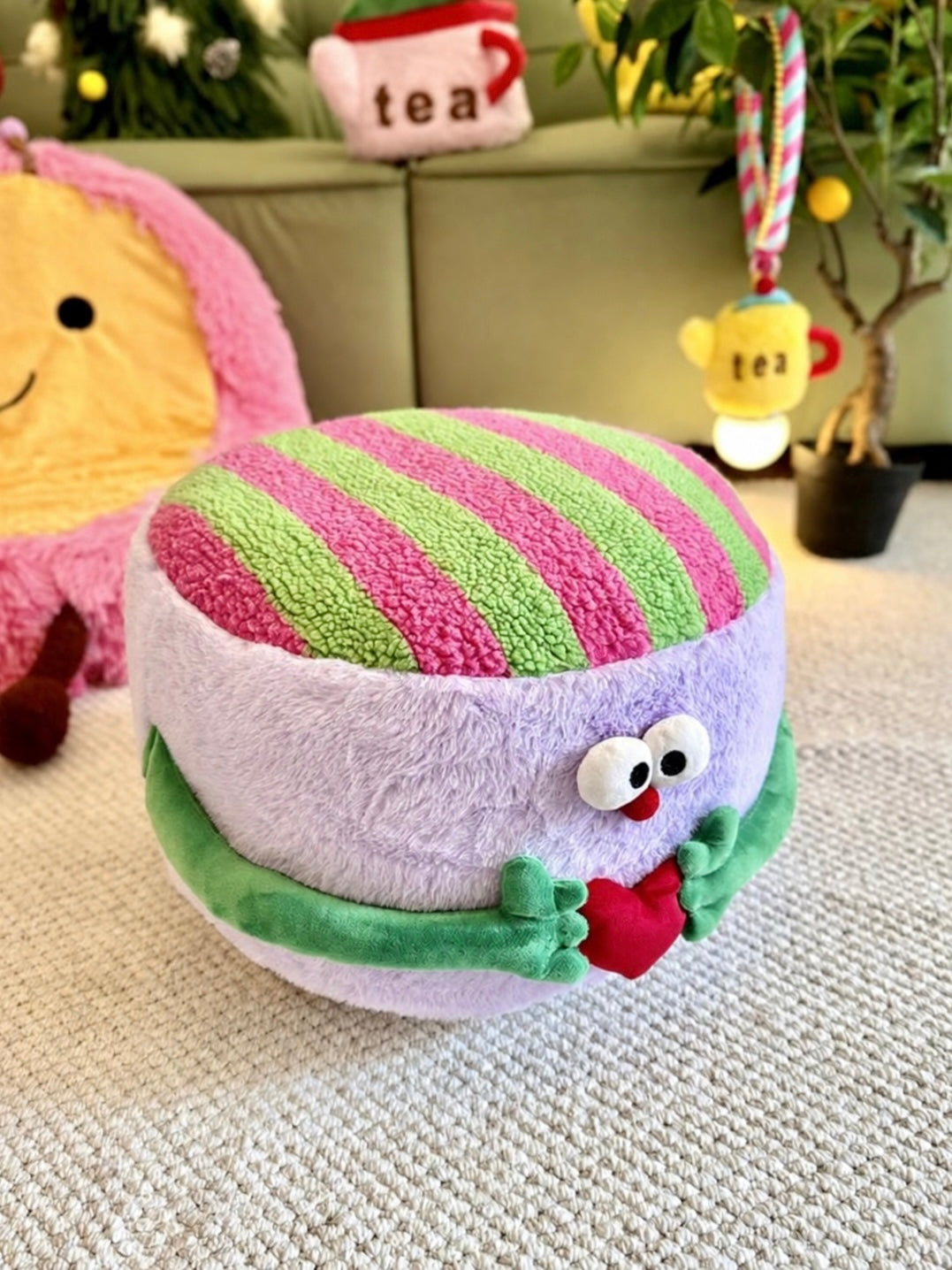 Purple plush footstool with striped top and green heart-holding arms